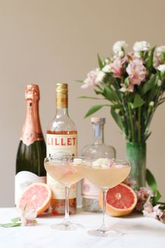 two wine glasses filled with pink grapefruit martinis next to bottles of booze and flowers