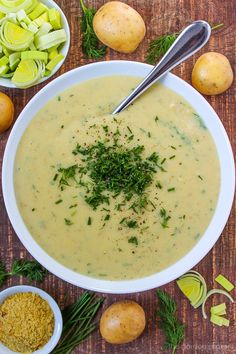 a white bowl filled with soup next to potatoes and celery on a wooden table