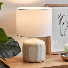 a white lamp sitting on top of a wooden table next to a vase and candle