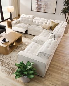 a large white couch sitting on top of a wooden floor next to a table with a potted plant