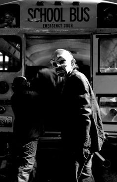 black and white photograph of two men standing in front of a school bus with the door open