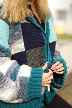 a woman with long blonde hair wearing a blue and black sweater holding a cell phone