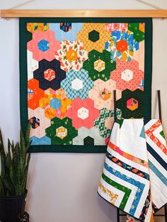 a colorful quilt hanging on the wall next to a potted plant and wooden rack