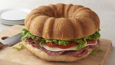 a bagel sandwich with meat, lettuce and tomatoes on it sitting on a cutting board