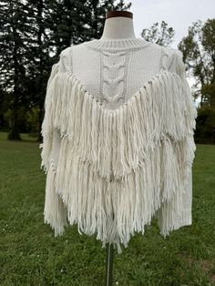 a white sweater with fringes sitting on top of a wooden stand in the grass