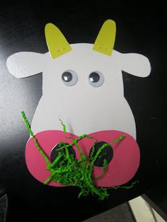 a cow made out of paper sitting on top of a black table next to a plant