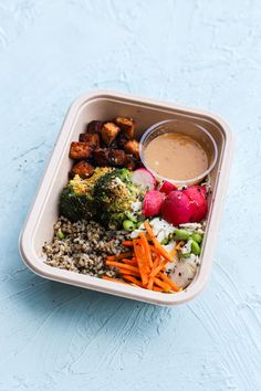 a container filled with lots of different types of food next to a cup of dipping sauce