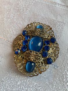 Gorgeous old Czech glass sash pin/brooch  Gold tone filigree setting with sapphire blue stones and cabochons  In very good condition, some discolouration on the back  It measures 6.2 cm x 5.2 cm Nice collectors piece Antique Blue Collectible Brooches, Luxury Blue Victorian Brooches, Luxury Antique Blue Brooches, Vintage Gold Brooch With Cabochon, Vintage Gold-tone Jewelry Brooch, Blue Stone, Czech Glass, Brooch Pin, Blue Sapphire