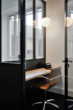 an office cubicle with a desk, chair and phone on the table in front of large windows