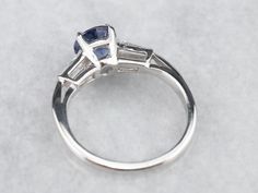 This vintage sapphire and diamond engagement ring is the epitome of a classic! This intense blue sapphire is a perfect, rich color, the benchmark for a fine sapphire. The crisp blue hue is filled with glitter and it has phenomenal light refraction, depth of color, and sparkle on the finger! We've set this in a tasteful platinum mounting featuring baguette diamonds on either side, equal in quality and sparkle to this lovely center sapphire. The ring was originally designed as an engagement piece, Classic Gia Certified Sapphire Ring, Platinum Sapphire Ring With Baguette Cut, Sapphire Baguette Cut Platinum Ring, Vintage Gia Certified Sapphire Ring, Baguette Cut Sapphire Platinum Ring, Timeless Round Cut Sapphire Ring, Classic Sapphire Tanzanite Solitaire Ring, Classic Sapphire Ring With Baguette Cut, Classic Tanzanite Solitaire Sapphire Ring