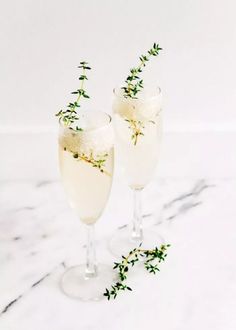 two glasses filled with white wine and garnished with small green sprigs