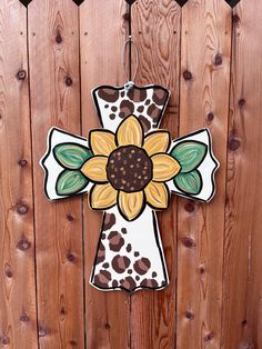 a wooden cross with a sunflower painted on the front and back of it, hanging from a wood fence