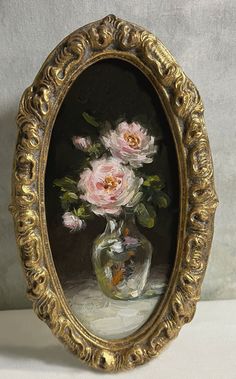 a painting of pink roses in a glass vase on a white tablecloth with a gold frame