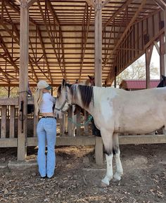 a woman standing next to a white and brown horse under a wooden structure with people in the background