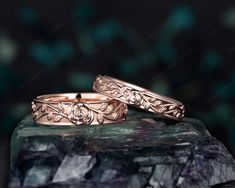 two gold wedding rings sitting on top of a green rock with leaves and scrolls in the middle