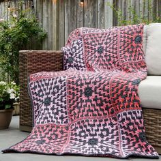 a pink and black blanket sitting on top of a couch next to a potted plant