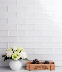 white roses in a vase next to a wooden box with pine cones on the side