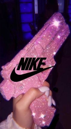 someone holding up a pink nike shoe with sparkles on the bottom and black nike logo above it