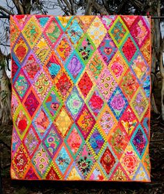 a colorful quilt hanging from a clothes line next to some tree's in the background