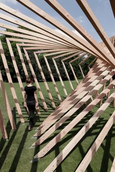 a woman walking through a wooden structure in the grass