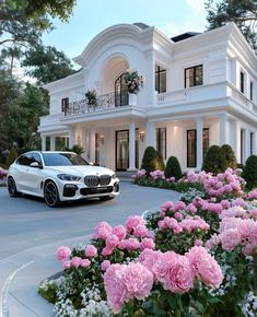 a white car is parked in front of a large house with pink flowers on the driveway