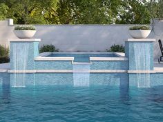 an outdoor swimming pool with water features and plants on either side, surrounded by white planters