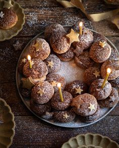 a plate filled with donuts covered in powdered sugar and topped with lit candles