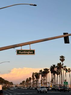 a street sign hanging from the side of a traffic light over a city street with palm trees