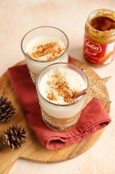 two glasses filled with drinks sitting on top of a wooden tray next to pine cones