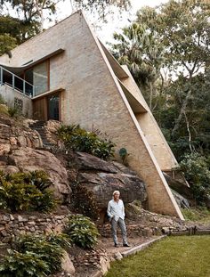 a man standing in front of a house on top of a hill next to trees