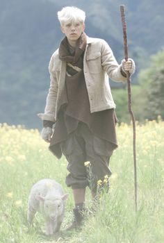 a woman holding a stick and walking next to a sheep