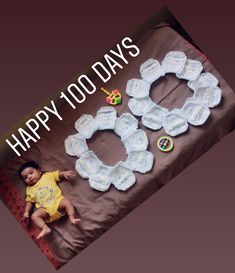 a baby laying on top of a blanket next to two diapers that say happy 100 days