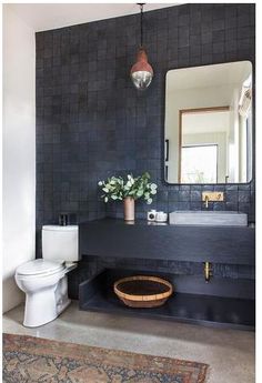 a bathroom with a toilet, sink and mirror in it's black tiled walls