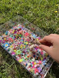 a person is holding a plastic container filled with small beads and other colorful objects in the grass