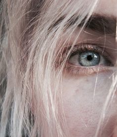 a close up of a person's eye with long blonde hair and blue eyes