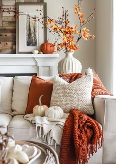 a living room filled with white furniture and fall decorations on top of each other in front of a fire place