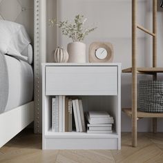 a white nightstand with books and vases on it next to a bed in a bedroom