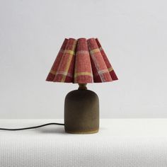 a lamp that is on top of a white tablecloth covered surface with a red and yellow checkered lampshade