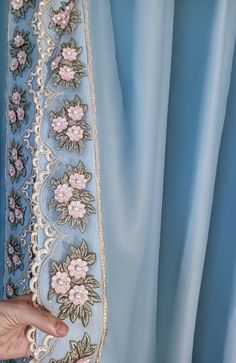 a hand is touching the edge of a blue curtain with pink flowers and leaves on it