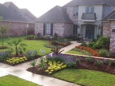 a house with landscaping in front of it and flowers around the lawns on either side