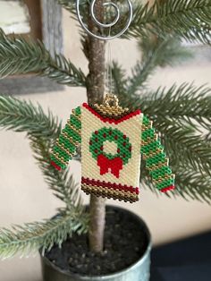 a christmas sweater ornament hanging from a tree in a pot with pine needles