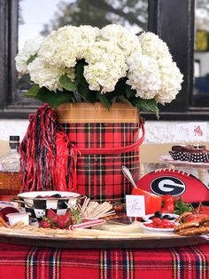 a table topped with a red and black plaid cloth covered vase filled with white flowers