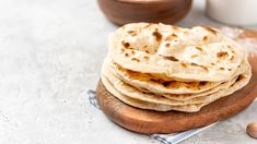 a stack of pita bread sitting on top of a wooden cutting board next to a glass of milk