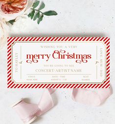 a merry christmas ticket sitting on top of a table next to some pink ribbon and flowers