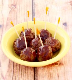 a yellow bowl filled with meatballs and toothpicks on top of a wooden table