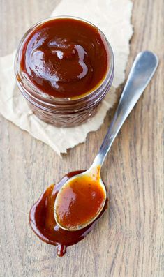 a spoon full of sauce sitting on top of a wooden table next to a jar