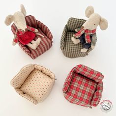 four small stuffed animals are sitting together in their bed bags, one is wearing a sweater and the other has a plaid coat