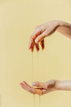 two hands reaching for some oil on a yellow background with one hand holding the other