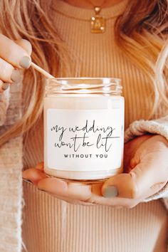 A lit candle with the phrase "My Wedding Won't Be Lit Without You," held by a woman in cozy attire, making it a perfect wedding favor. Elegant Bridesmaid Proposal, Creative Bridesmaid Proposal Ideas, Modern Bridesmaid Proposal, Font Minimalist, Bridesmaid Proposal Candle, Unique Calligraphy, Minimalist Candle, Candle Favor, Bridesmaid Candle