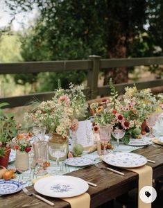 a long table with plates and flowers on it is set for an outdoor dinner party